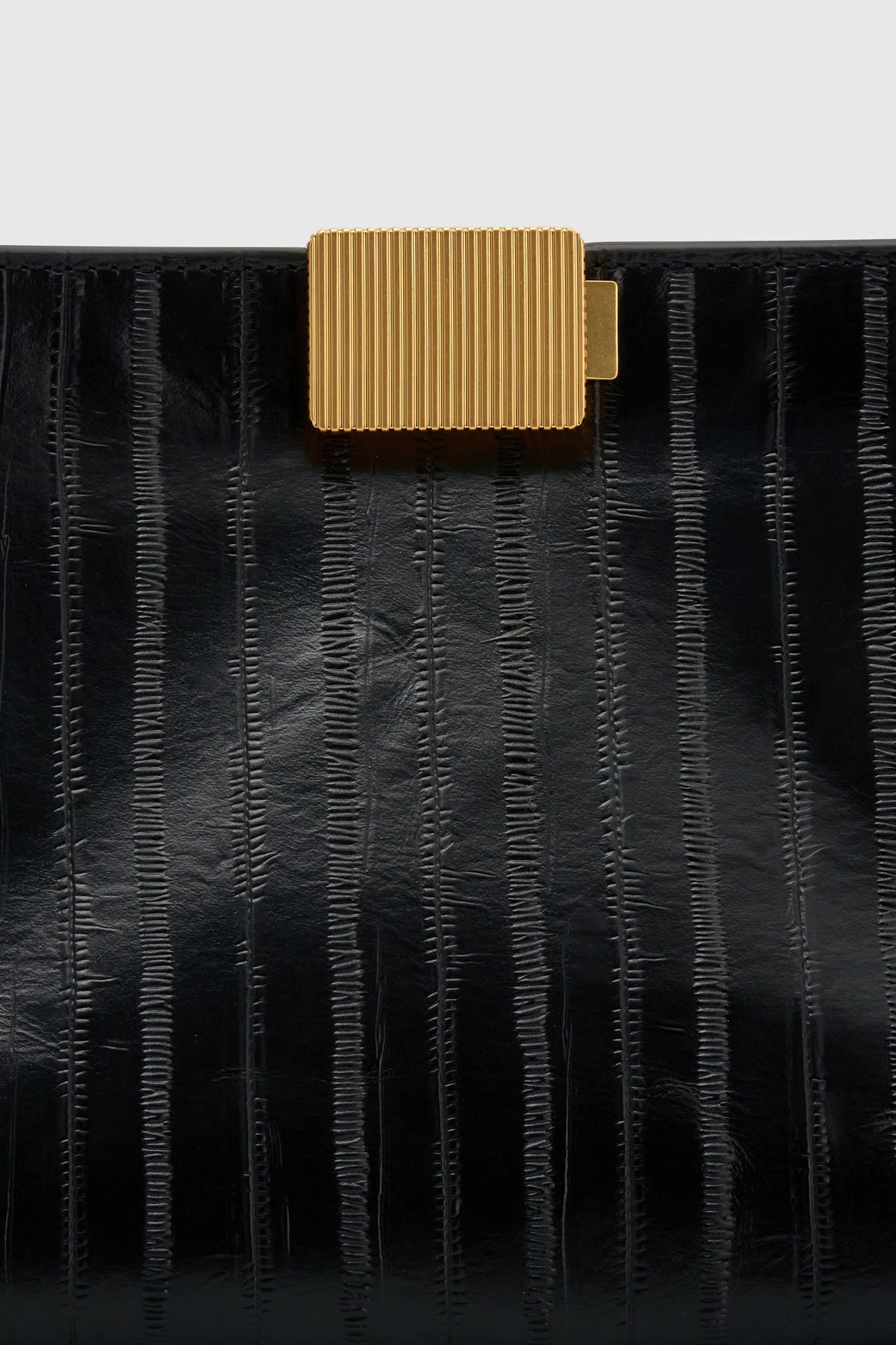 Cropped view CAMILLA AND MARC Poppy Eel Clutch in Black eel‑embossed leather with ribbed gold hardware.