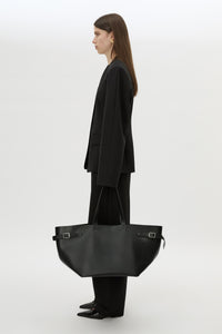 Front styled view CAMILLA AND MARC Willa Tote in Black with side strap and buckle detailing and magnetic button closure.